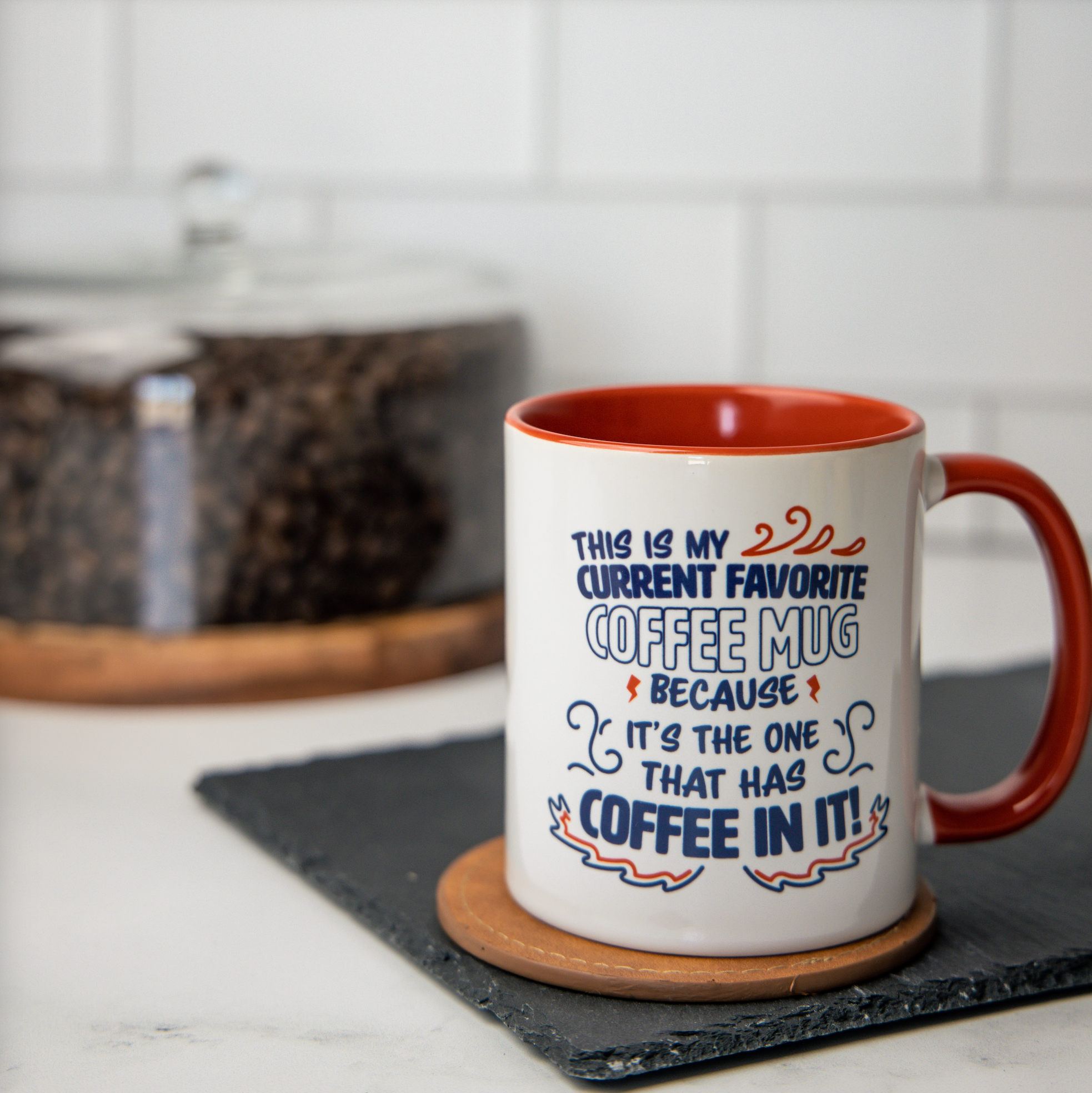 White 11oz mug with Navy text reads “This is my current favorite coffee mug because it’s the one that has coffee in it!” Red handle, interior Lifestyle background